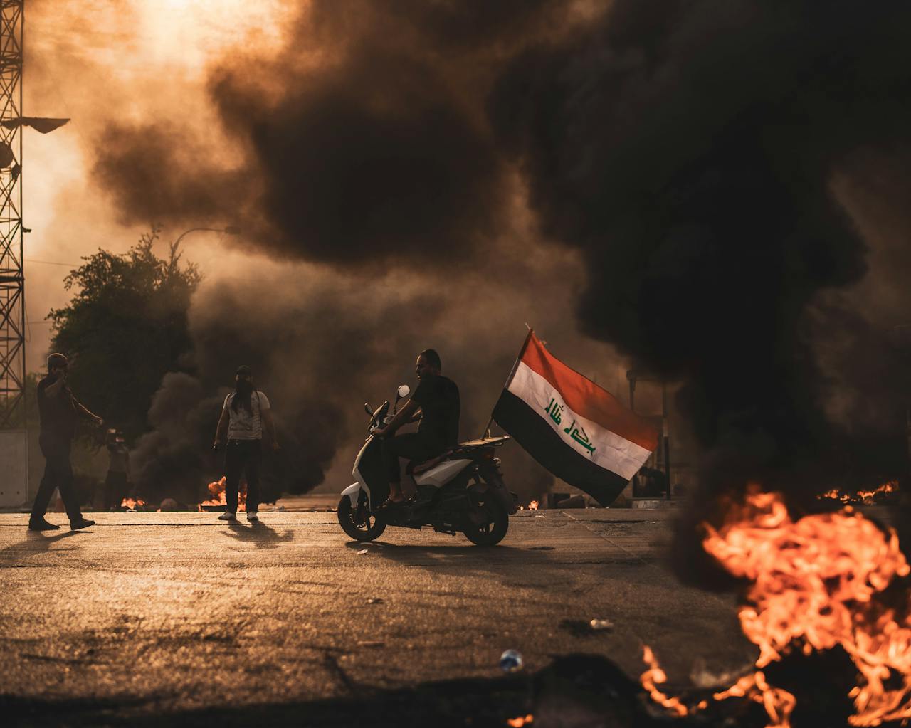 Intense protest scene with people on motorbikes, smoke, and flames, showcasing civil unrest.