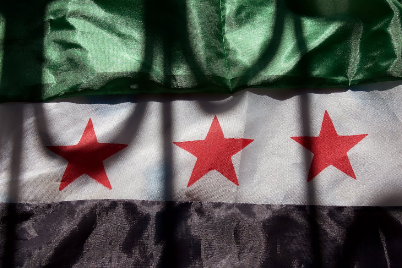A close-up of the Syrian flag showing green, white, and black stripes with red stars.