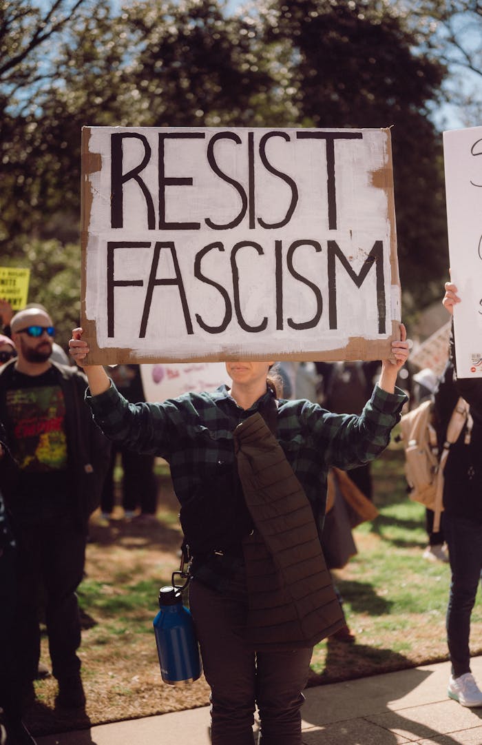 Protester holding a 'Resist Fascism' sign at an outdoor rally.