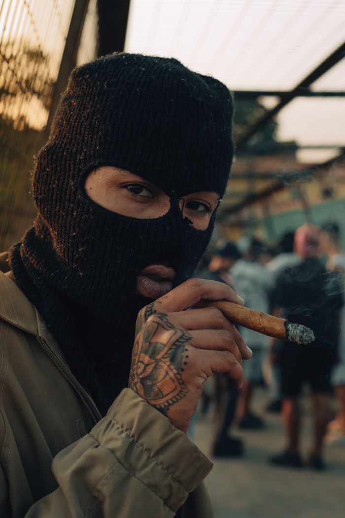 Close-up of a person wearing a balaclava and smoking a cigar outdoors, adding mystery and intrigue.