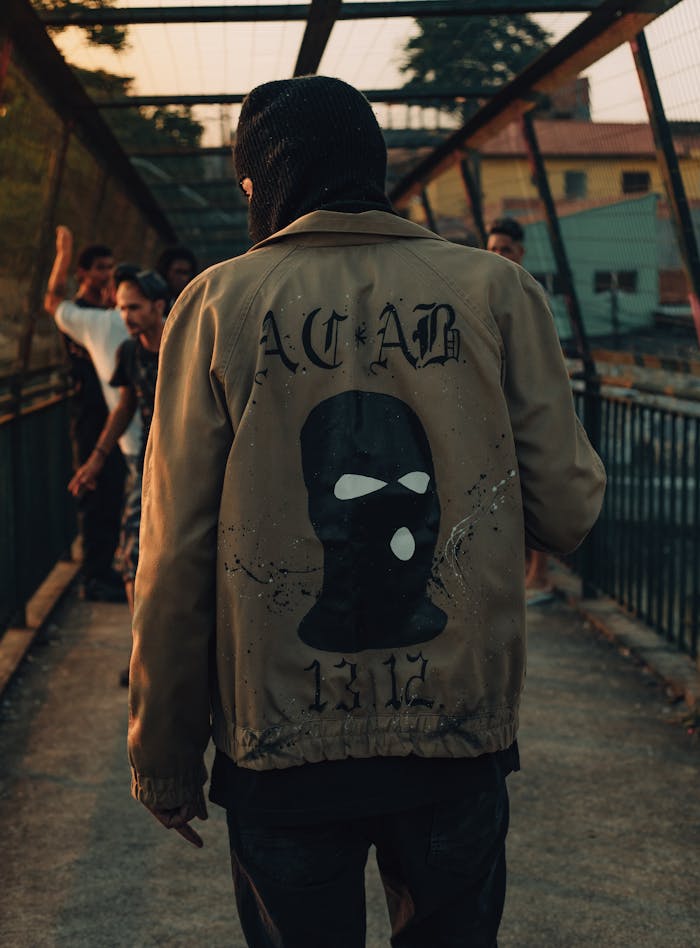 Man in jacket with balaclava design walking on a bridge at sunset